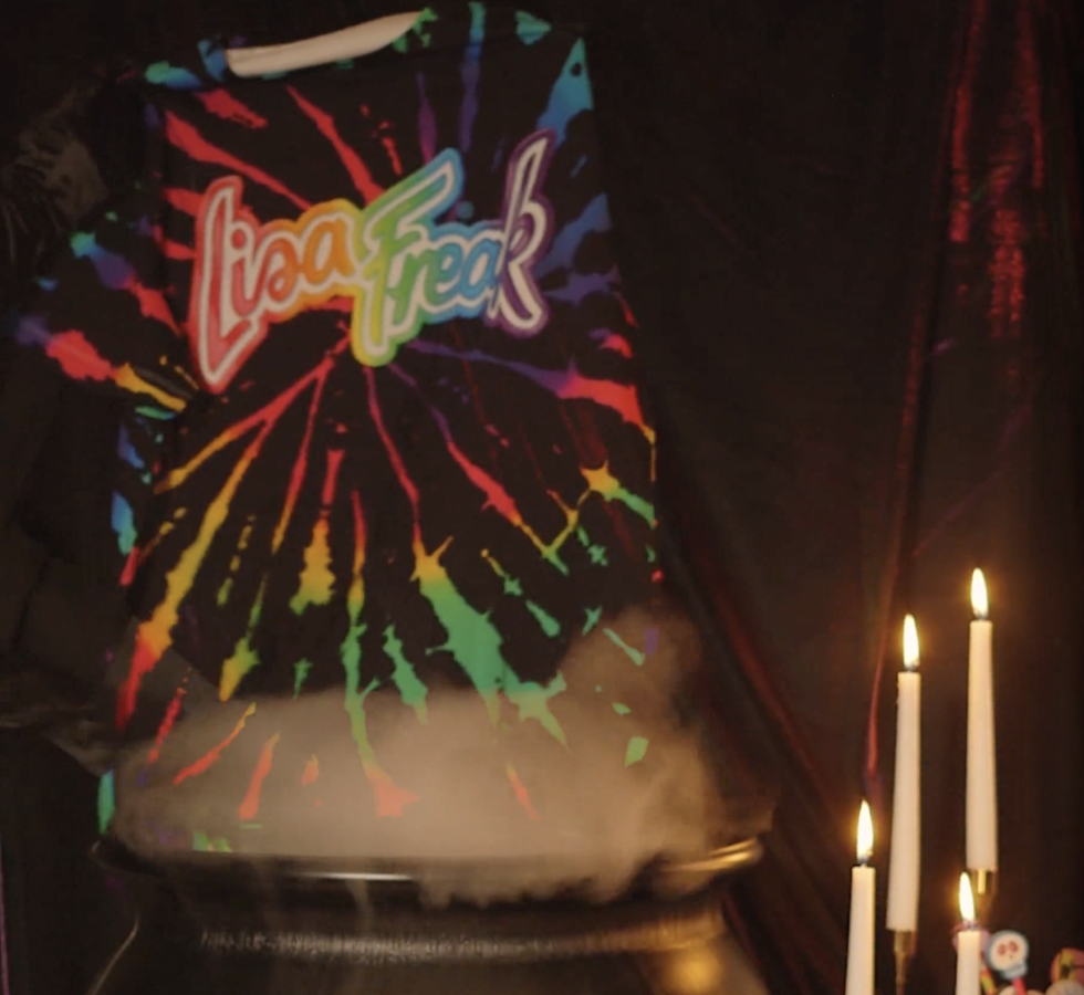 A tie-dye hoodie with the Lisa Freak logo entering a Halloween witch's cauldron.